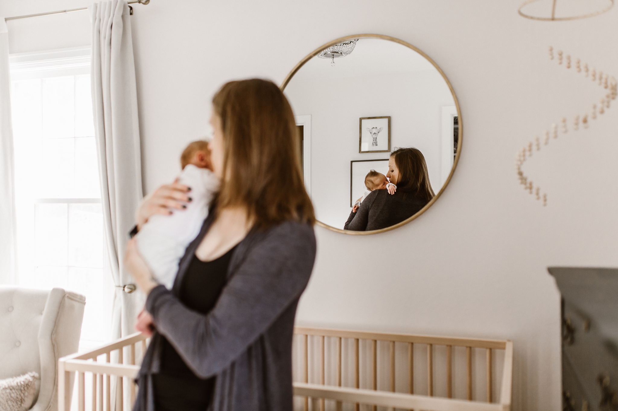 Mirror reflection of a mother holding her baby in the nursery.